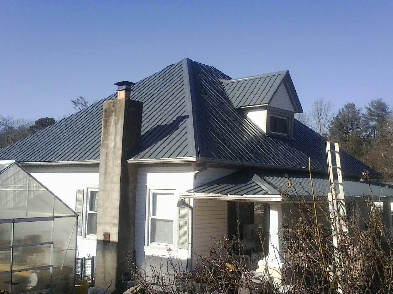 Dark blue standing seam metal roof on a white farmhouse with dormer — Slate & Tile Roof Repair by Roofing Brothers in Absarokee
