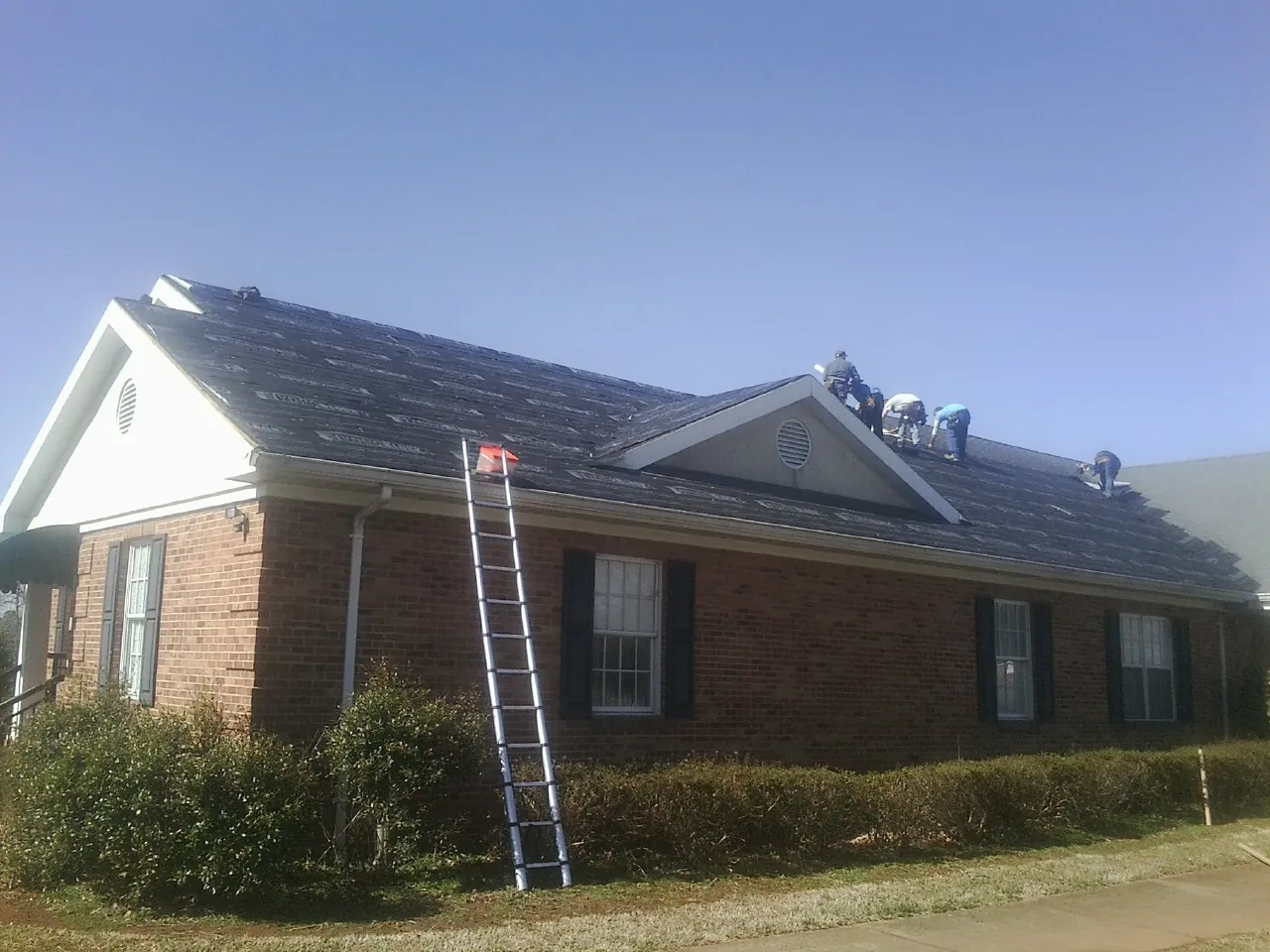 Crew tearing shingles off a brick ranch roof with a ladder set — Emergency Roof Repair work by our crew in Absarokee