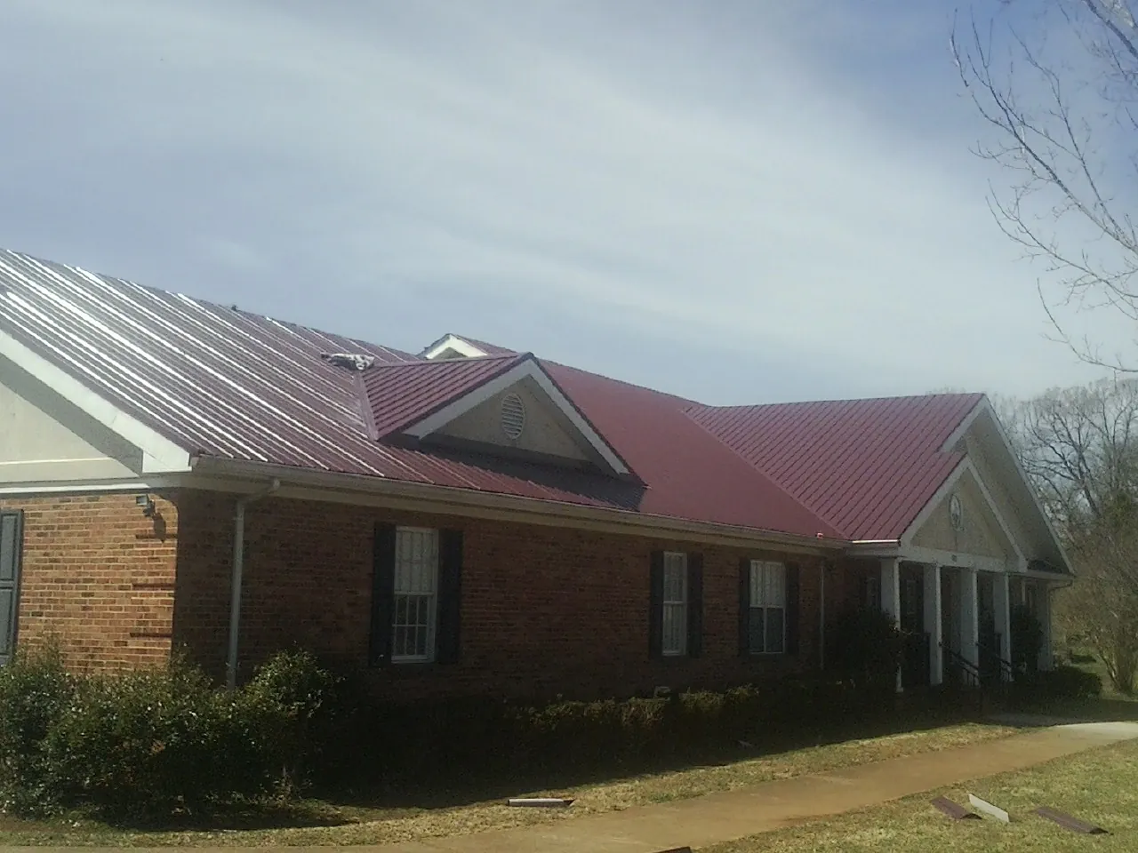 Red metal roof with gabled entries on a long brick building, from a Hail Damage Roof Repair job in Absarokee