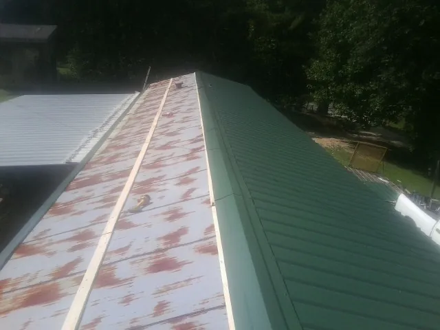 Old rusted panels beside newly installed green metal roofing — Wind Damage Roof Repair by Roofing Brothers in Absarokee