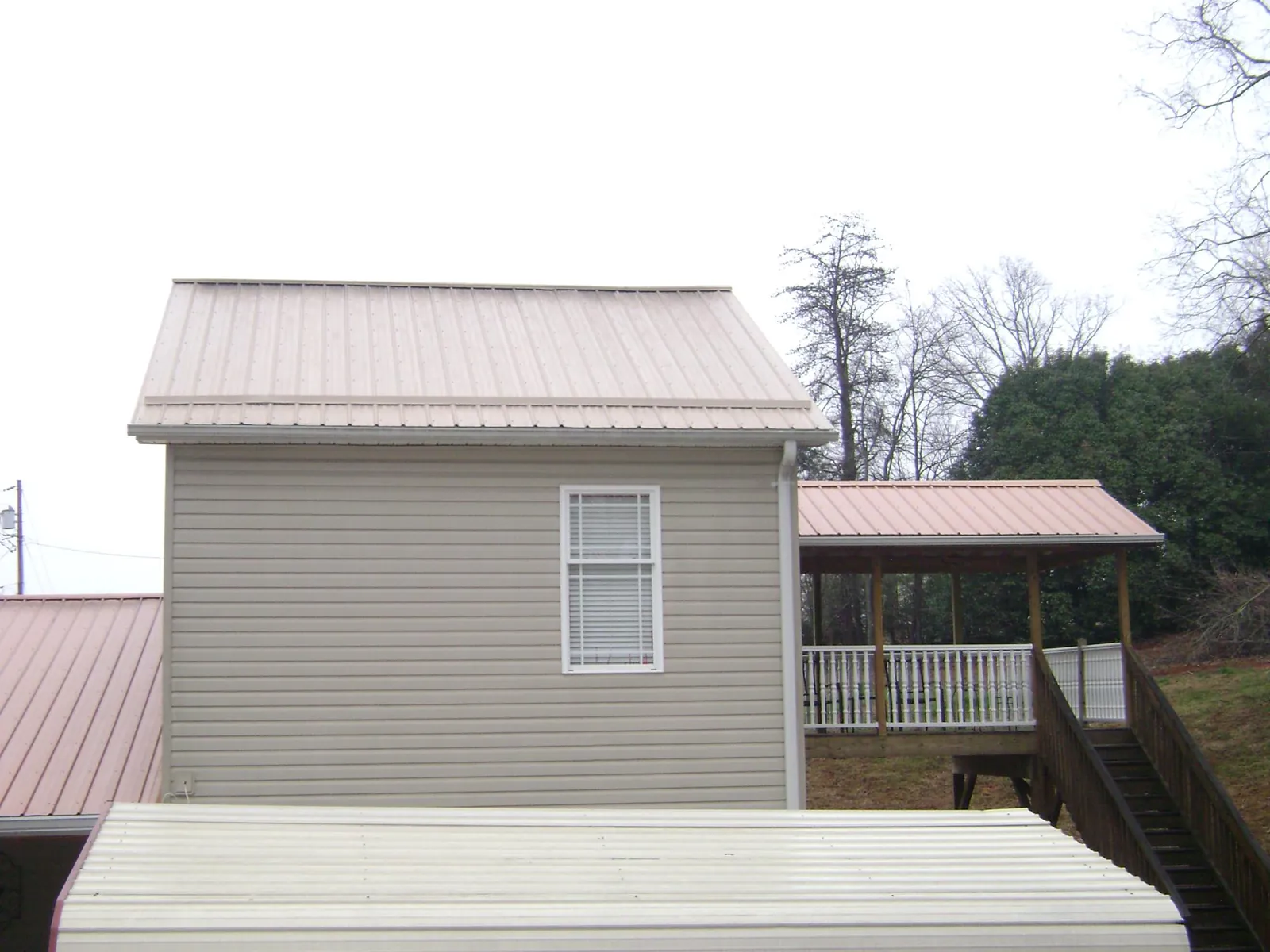 Tan metal roofs on a two story addition and attached porch, from a Roof Replacement job in Absarokee